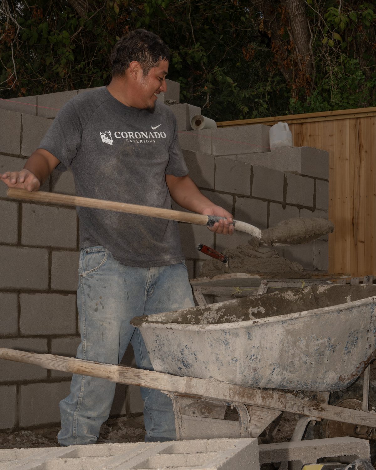 Coronado Exteriors crew member shoveling mortar on a concrete block wall jobsite