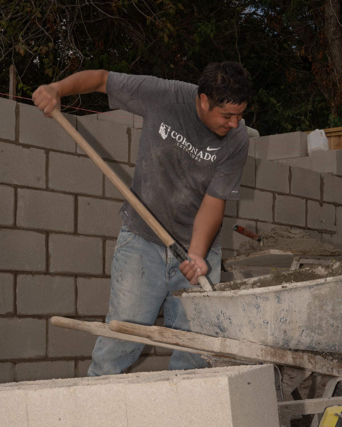 Coronado Exteriors mason in a company shirt mixing mortar beside a CMU block wall